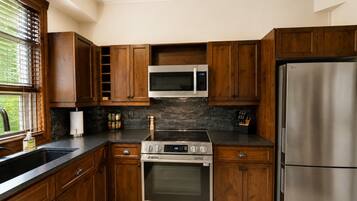 Una cocina con armarios de madera, un refrigerador de acero inoxidable, un microondas, un horno y un lavamanos.