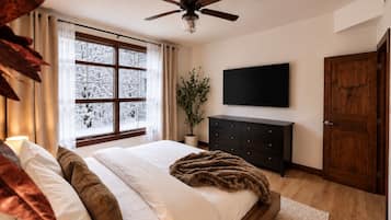 Un dormitorio con cama, ventilador de techo, televisor montado en la pared, cómoda de madera y una puerta.