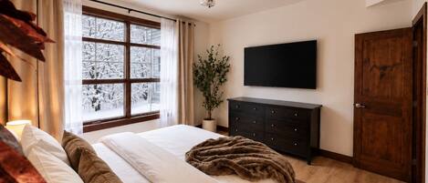 Une chambre à coucher comprenant un lit, un ventilateur de plafond, un téléviseur fixé au mur, une commode en bois et une porte.