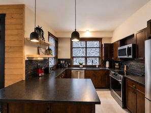 Eine moderne Küche mit dunklen Arbeitsplatten, Holzschränken, einem Edelstahlkühlschrank und einem eingebauten Backofen.