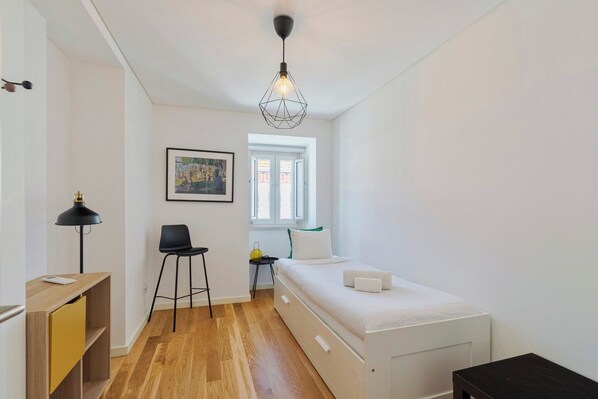 Ein Schlafzimmer mit Bett, Schreibtisch, Stuhl, Lampe und Fenster.