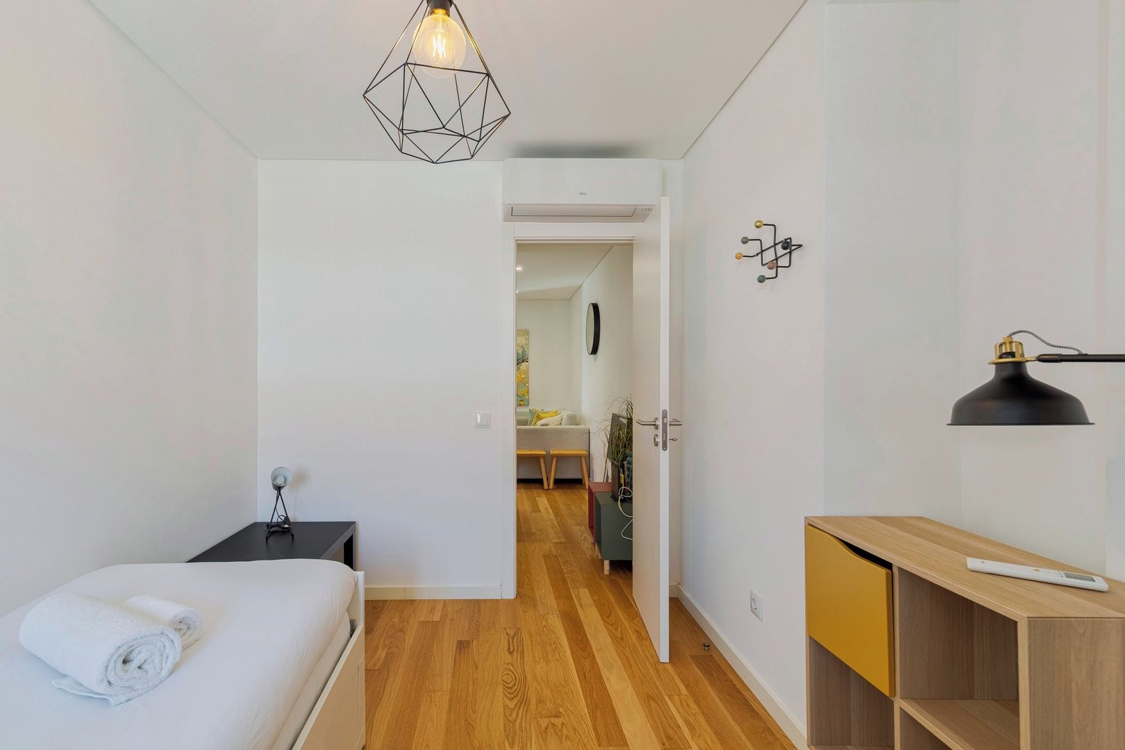 A modern bedroom with a bed, bedside table, lamp, and a geometric pendant light.
