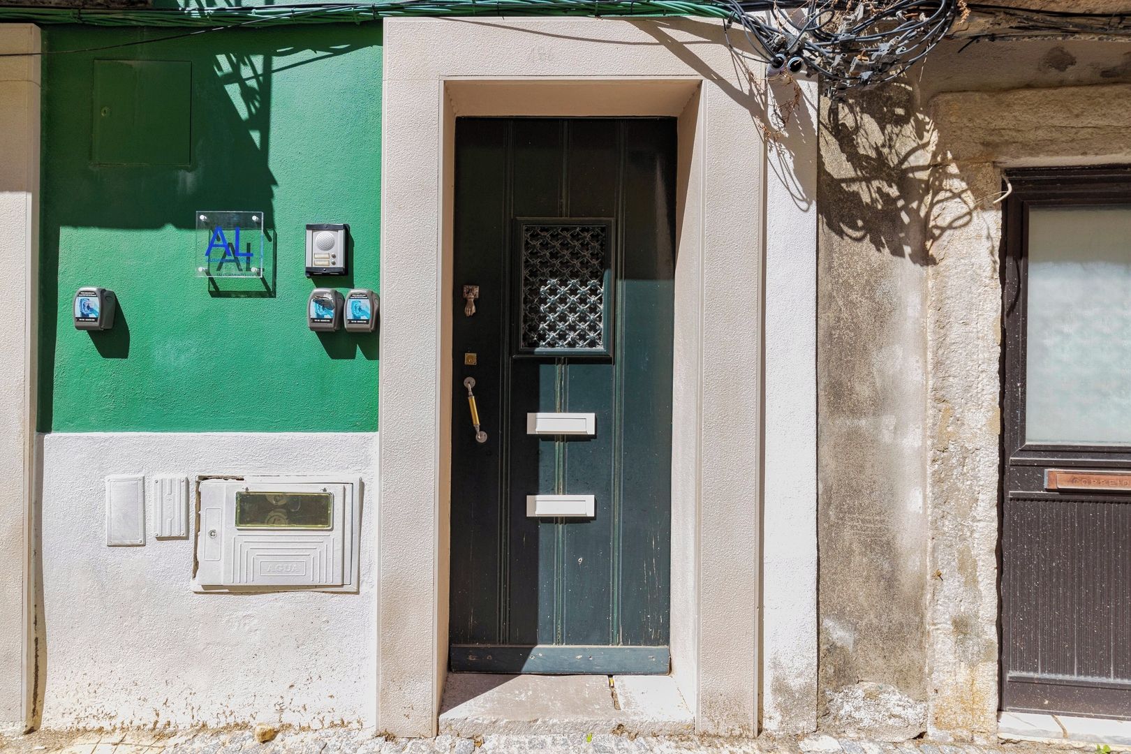 A building facade with a green wall, a black door with a metal grid, and two security cameras mounted on the wall.