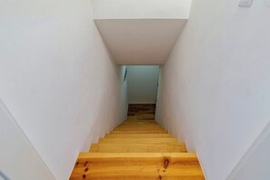 Eine schmale, hölzerne Treppe führt zu einem Zimmer mit weißen Wänden und Holzboden.