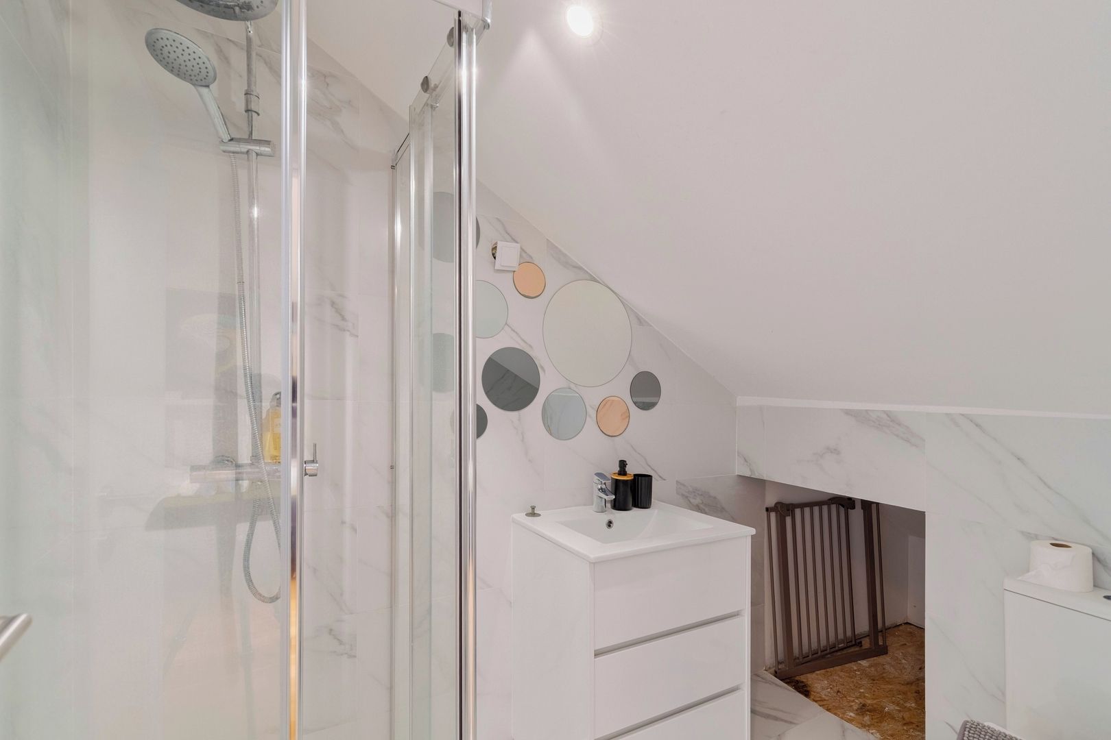 Ein modernes Badezimmer mit Duschkabine aus Glas, einem weißen Waschbecken mit Spiegel darüber und einer Wand mit runden Spiegeln.