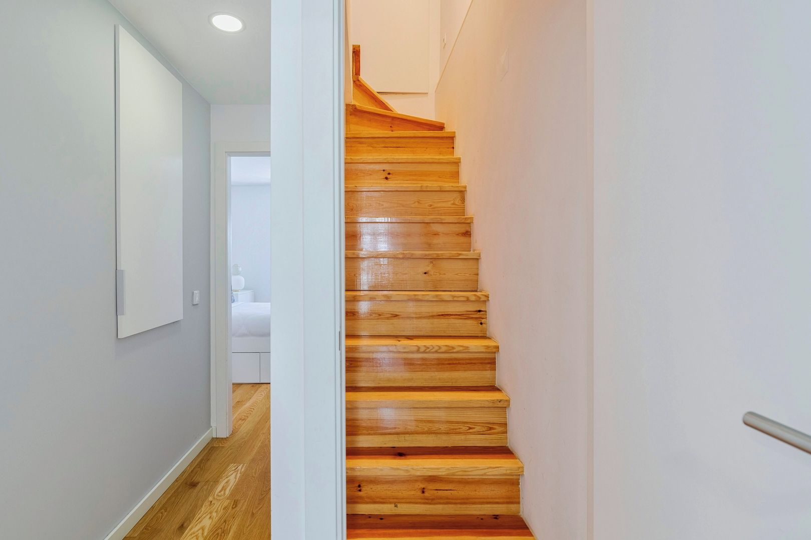 A wooden staircase leading to a bedroom with white walls and a wooden floor.