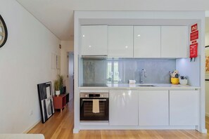 A modern kitchen with white cabinets, a built-in oven, and a glass backsplash. - Blue Coconut Second, By Home Match (Setúbal)