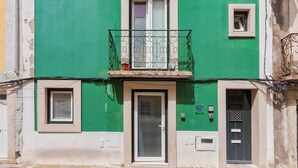 A building with a green facade, a balcony with ornate metal railings, and a door with a window above it. - Blue Coconut RC 188, By Home Match (Setúbal)