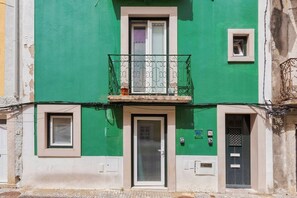 Ein Gebäude mit grüner Fassade, einem Balkon mit aufwendigen Metallgeländern und einer Tür mit Fenster darüber.