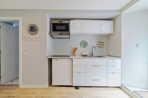 A compact kitchen with white cabinets, a microwave, and a sink. There are decorative plates on the wall and a coat rack with hooks. - Blue Coconut RC 188, By Home Match (Setúbal)