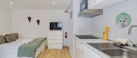 Habitación compacta con cama, televisión, kitchenette con pileta y extintor.