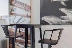 Ein moderner Essbereich mit einem schwarzen Tisch und Stühlen, einem Heizkörper und einer Wand mit einem großen Gemälde von Delfinen.