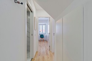 A narrow hallway with wooden flooring, white walls, and a door leading to a room with a window. - Blue Coconut First, By Home Match (Setúbal)