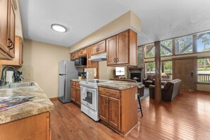 A spacious kitchen with wooden cabinets, a stainless steel refrigerator, a microwave, and a stone fireplace. - Peaceful Retreat Mins to Silver Dollar City&Table Rock Lake_Free Attraction Tickets_Cmty Pools (Branson)