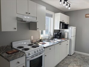 A modern kitchen with white cabinets, a stove, a microwave, and a refrigerator.
