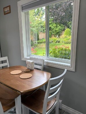 A dining area with a round table, white chairs, and a window with a view of a garden.