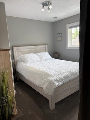 A bedroom with a bed, a nightstand, a lamp, and a window.