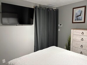 A bedroom with a bed, a dresser, a television mounted on the wall, and a framed picture.