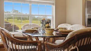 Un coin repas avec des chaises en osier, une table en verre et une vue dégagée sur l’extérieur grâce à une grande fenêtre.