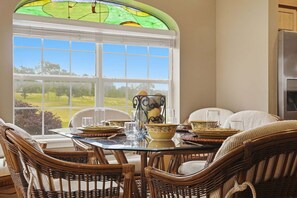 A dining area with wicker chairs, a glass table, and a view through a large window. - Perfect Central Branson Stay Golf Course View • Show Discounts (Branson)
