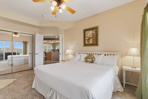 Une chambre d’hôtel avec un grand lit, un ventilateur de plafond, un tableau au mur et une vue sur l’extérieur par une porte ouverte.