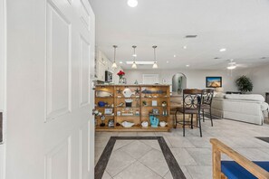 A modern living room with a wooden display shelf, a white sofa, and a dining area with a table and chairs. - Beach Bungalow - Historic American Beach - 3 Bedrooms, 3 Bathrooms (Fernandina Beach)
