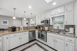 A modern kitchen with white cabinets, stainless steel appliances, and a tiled backsplash. - Beach Bungalow - Historic American Beach - 3 Bedrooms, 3 Bathrooms (Fernandina Beach)