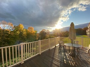 Une terrasse en bois avec une balustrade blanche, une table ronde entourée de chaises et un parasol.