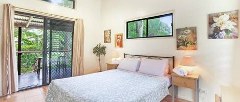 A bedroom with a bed, a nightstand, a window, and a door leading to a balcony.