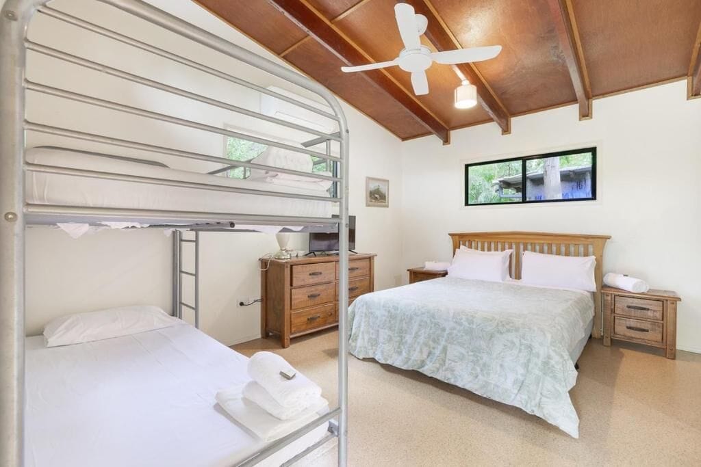 A bedroom with bunk beds, a single bed, wooden nightstands, a ceiling fan, and a window with a view.