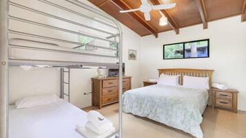 A bedroom with bunk beds, a single bed, wooden nightstands, a ceiling fan, and a window with a view.