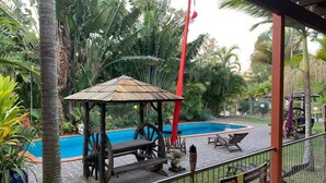 Una zona de piscina con una estructura de madera, sillas de descanso y un jardín cercado.