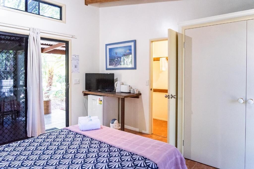 A bedroom with a bed, a desk with a computer, a window, and a door.