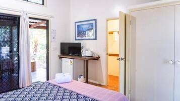 A bedroom with a bed, a desk with a computer, a window, and a door.