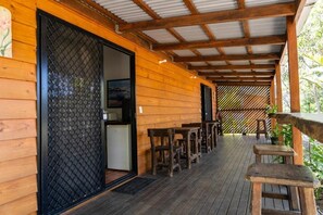 Une terrasse en bois avec des sièges d’extérieur, une porte-fenêtre coulissante et un espace abrité doté d’un toit en métal.