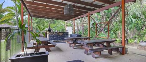 Un patio al aire libre con mesas de picnic, una lámpara colgante y un menú en una pizarra.