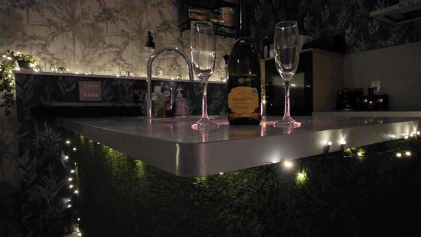 A bar area with a marble countertop, two wine glasses, a bottle of Prosecco, and a decorative plant.