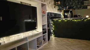 A modern kitchen with a built-in TV, a bar area with string lights, and a herringbone floor pattern.