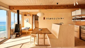 Ein geräumiges Zimmer mit einem großen Holztisch, einer Küchenzeile und Blick auf das Meer.