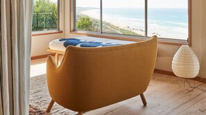 Ein Zimmer mit großem Fenster mit Blick auf einen Strand, Holzboden und einem einzelnen Sessel.