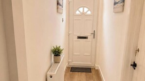 A hallway with a white door, a radiator, a potted plant, and a doormat. - Manchester Oasis - Spacious 4 Bedroom House (Manchester)