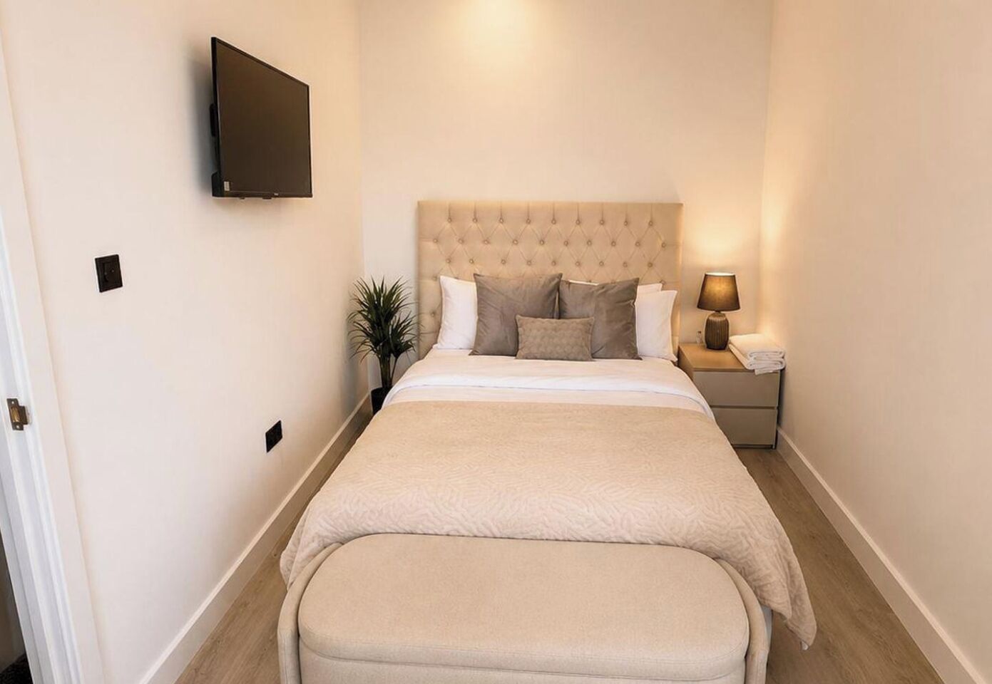 A hotel room with a bed, bedside table, lamp, and a wall-mounted TV.