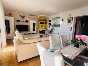 A modern living room with a sofa, TV, dining table, and decorative plants. - A6 - Spacious apt w pool, terrace and sea view (Dugi Rat)