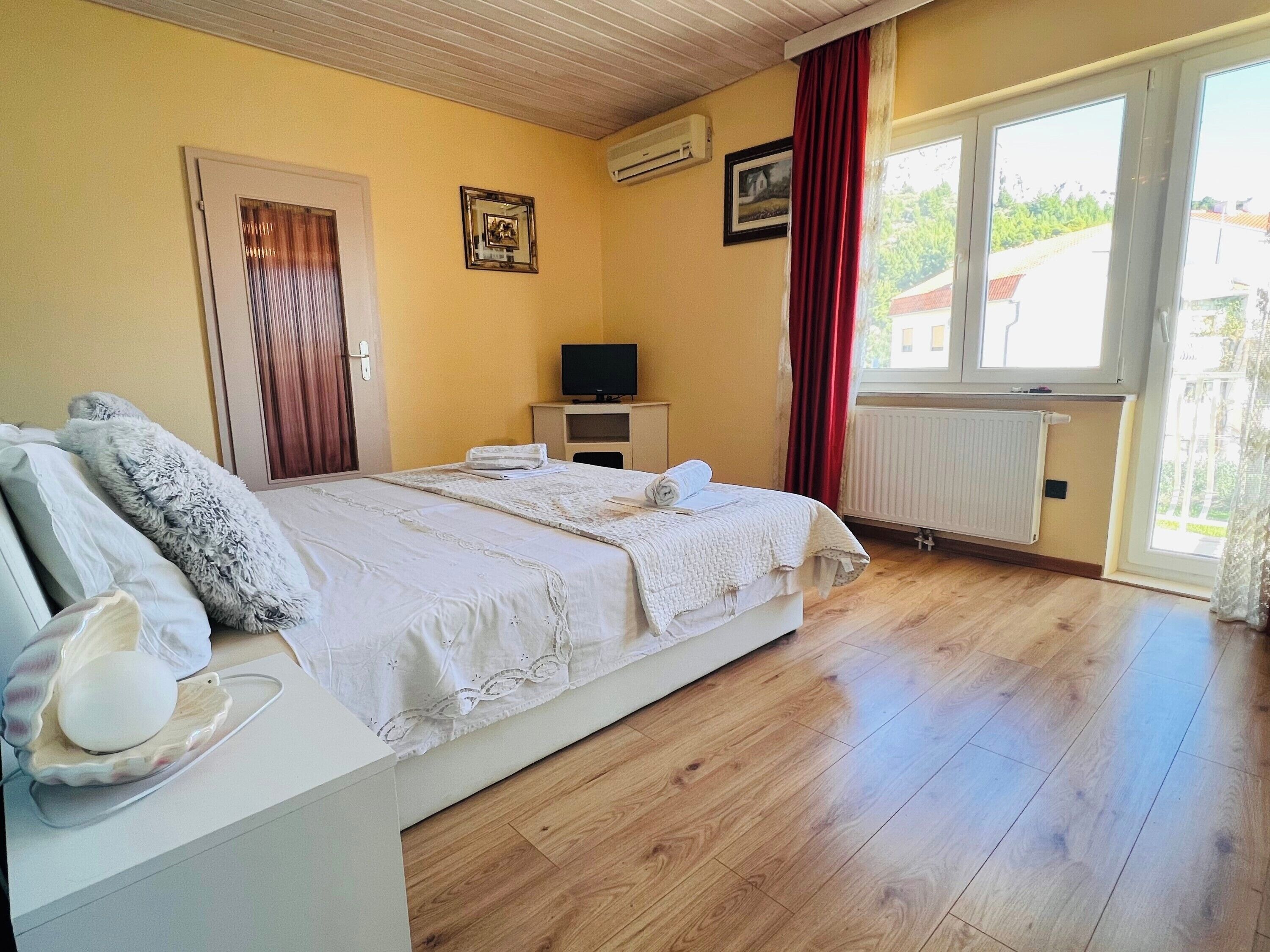 A bedroom with a bed, a television, a radiator, and a window with curtains.