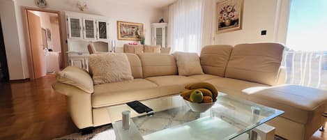 A living room with a beige sofa, a glass coffee table with a bowl of fruit, and a white cabinet in the background.