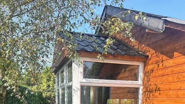 A wooden cabin with a glass door, surrounded by wooden barrels and potted plants. - Gortin Glen Forest Cabin, Sleeps 7 with Parking (Omagh)