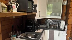 A compact kitchen with a microwave, coffee maker, and wine glass. - Gortin Glen Forest Cabin, Sleeps 7 with Parking (Omagh)