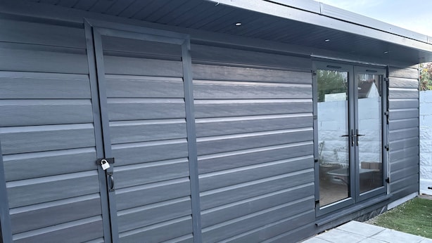 A modern building with horizontal siding, a sliding glass door, and a small patio area.