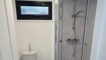 Une salle de bain équipée de toilettes, d’une fenêtre, d’une douche et d’un rouleau de papier toilette.