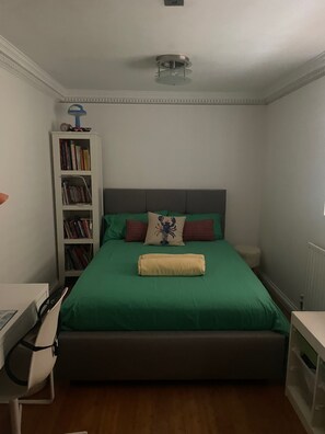Een slaapkamer met een bed, een boekenkast, een bureau en een radiator.